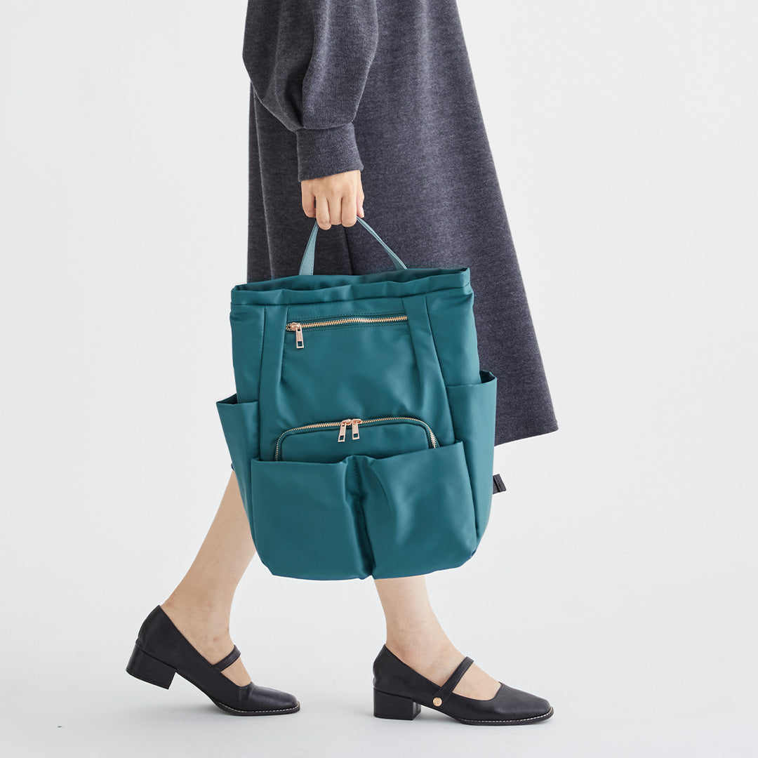 グリーンWポケットナイロンリュックを手に持つ女性