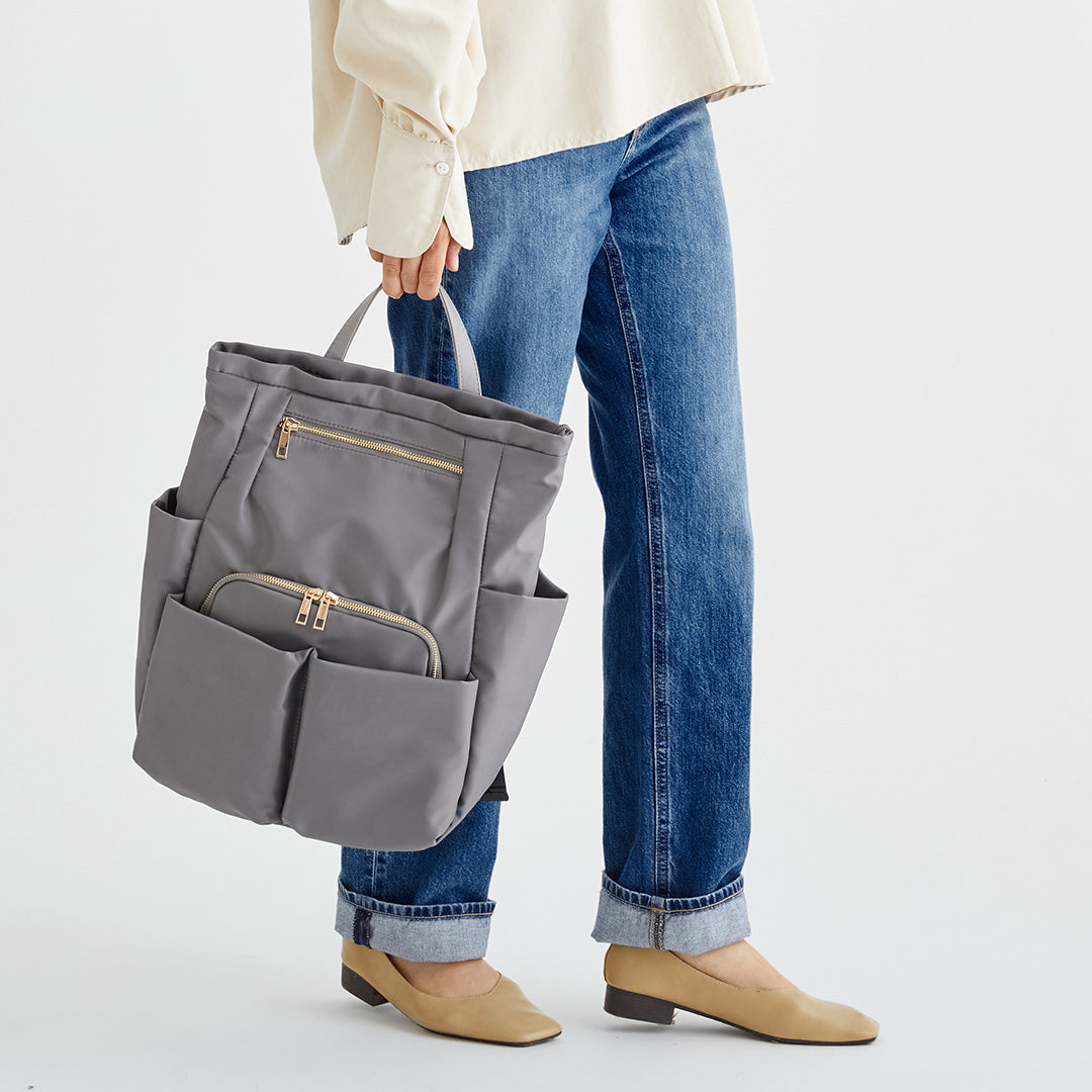 グレーWポケットナイロンリュックを手に持つ女性