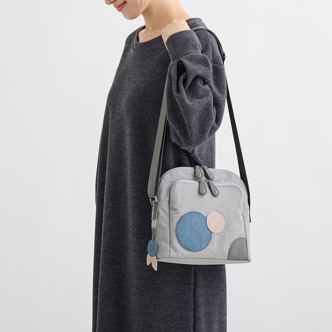 グレーの水玉ナイロンショルダーバッグを肩にかけた女性