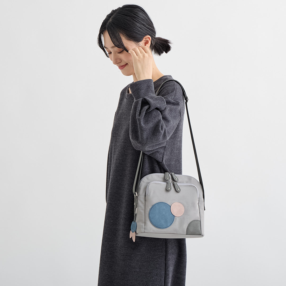 グレーの水玉ナイロンショルダーバッグを肩にかけた女性