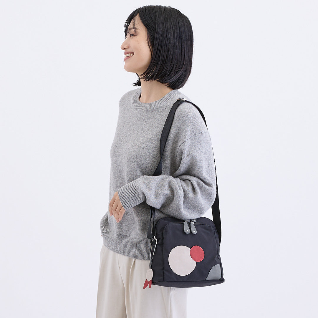 ブラックの水玉ナイロンショルダーバッグを肩にかけた女性