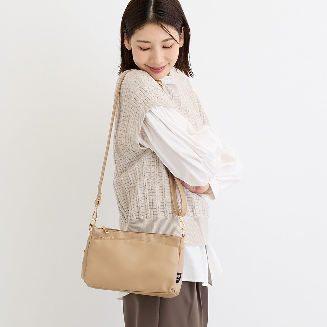 ベージュ合皮ショルダーバッグを肩掛けする女性
