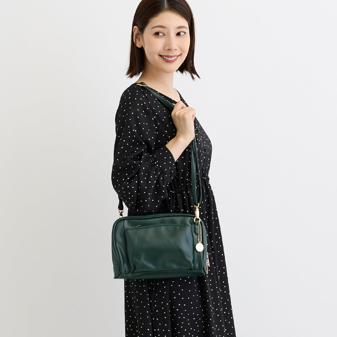 グリーンの合皮ショルダーバッグを肩掛けした女性