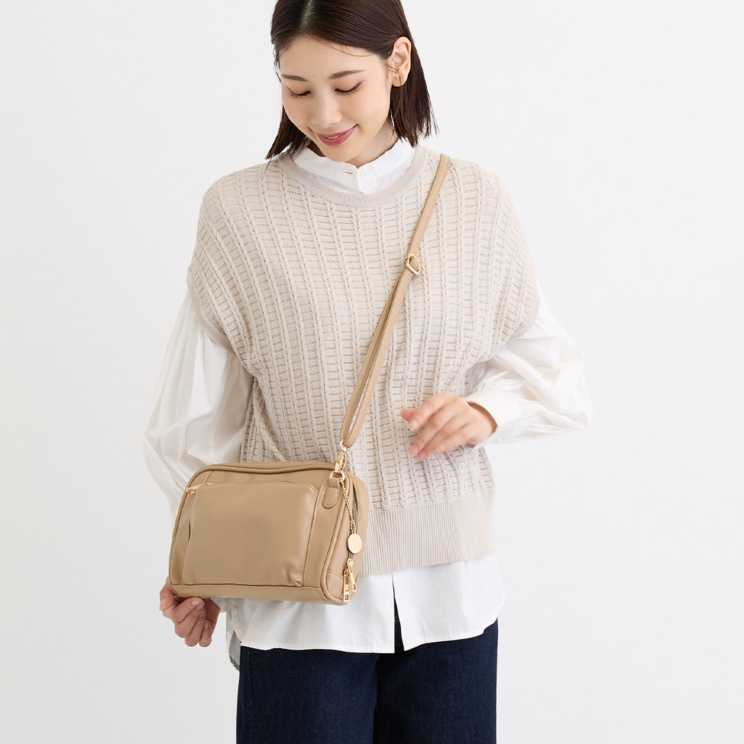 ベージュの合皮ショルダーバッグを肩掛けした女性