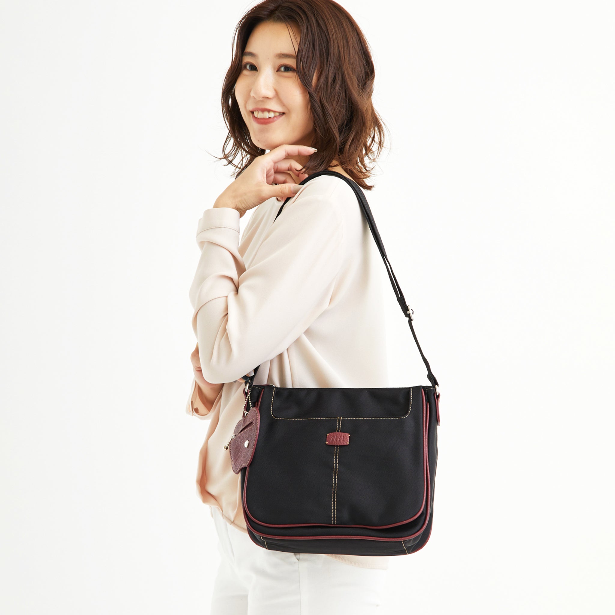 シワナイロンリンゴチャーム付きショルダーバッグ ブラックレッドを肩掛けした女性モデル