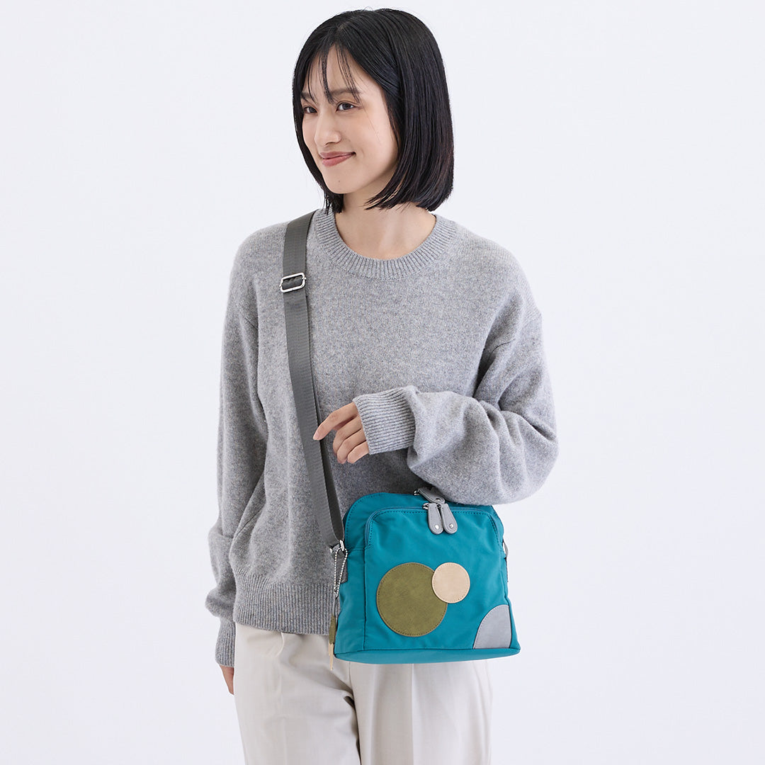 ブルーの水玉ナイロンショルダーバッグを肩にかけた女性