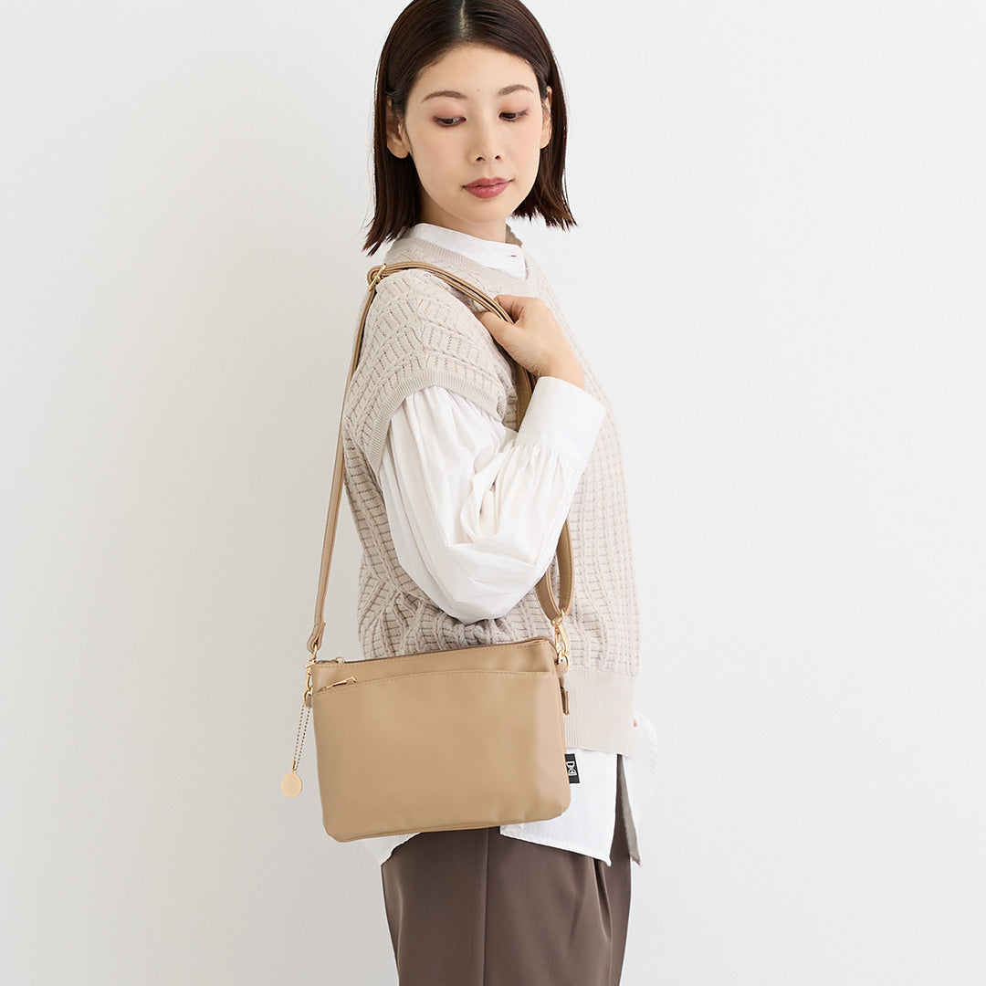 ベージュ合皮ショルダーバッグを肩掛けする女性