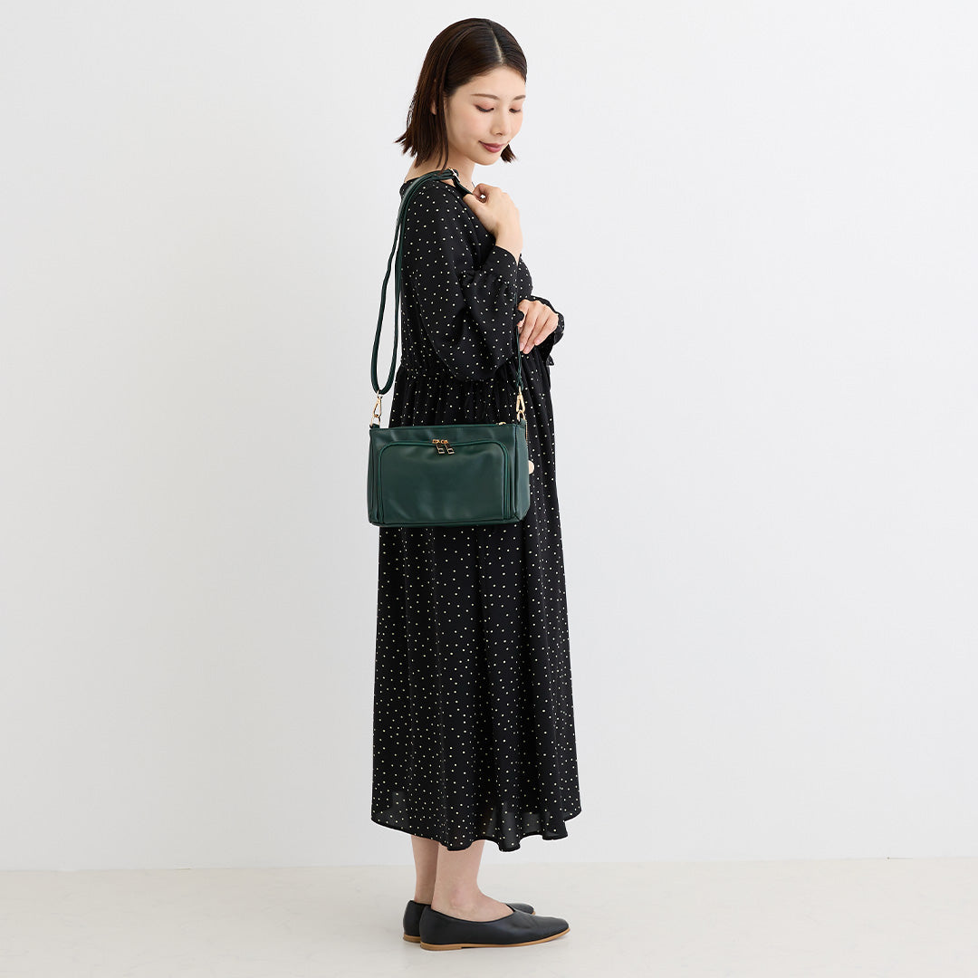 グリーンの合皮ショルダーバッグを肩掛けした女性